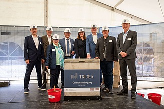 Foto von mehreren schick gekleideten Personen mit Helm vor einem Pult. 