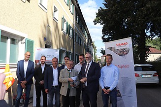 Foto von mehreren Personen, die vor einem gelben Gebäude stehen, hinter ihnen sind zwei Roll-ups