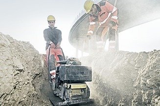 Photo of two construction workers with a machine doing civil engineering work in a trench