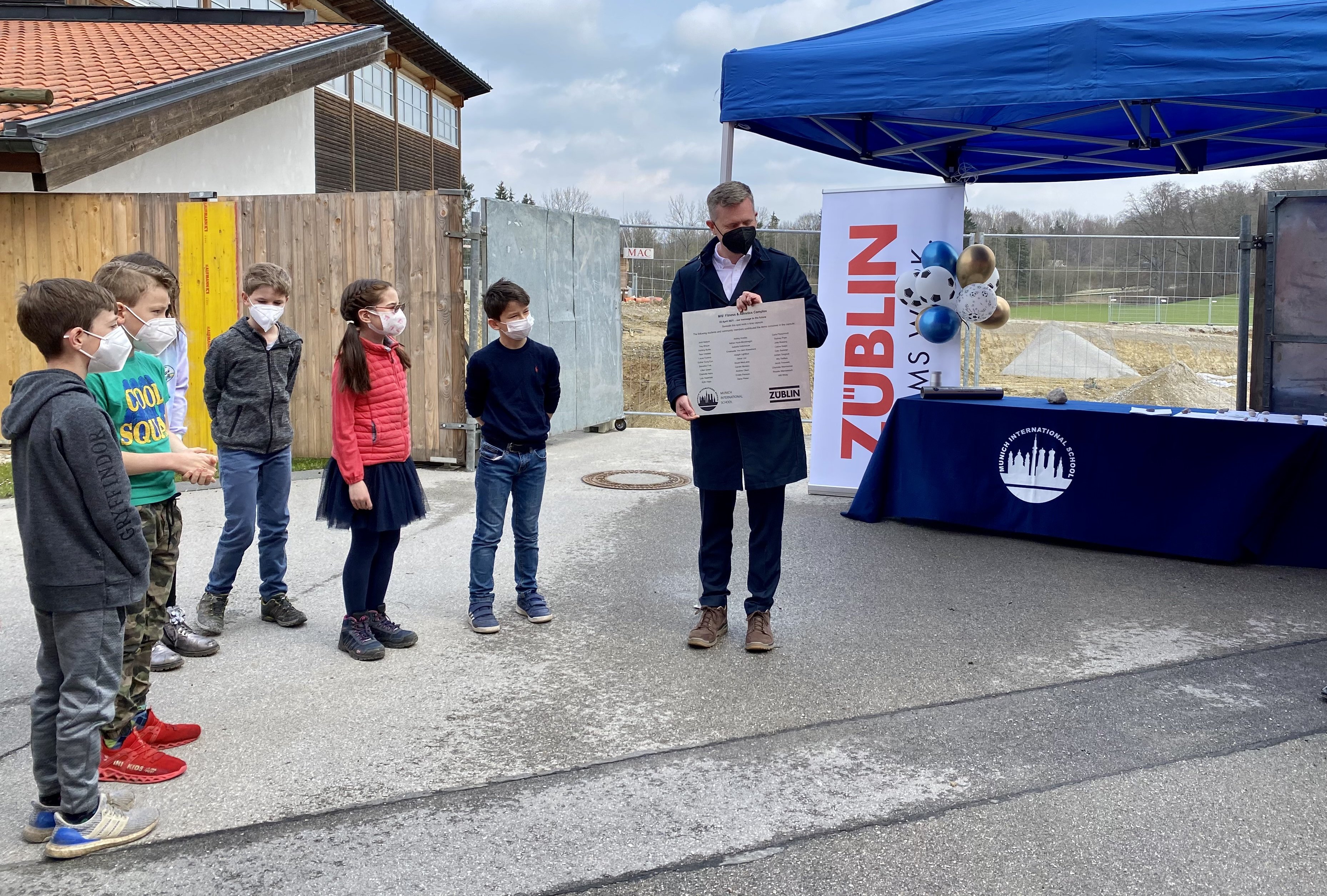 Foto von Kindern und einem Mann, die an einer Zeitkapsel-Zeremonie teilnehmen. 