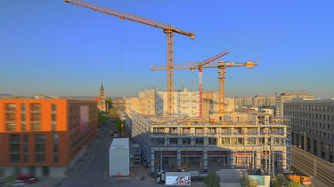 Foto von einer Baustelle für Wohnungen, mit drei Kränen.  