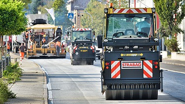 Das Bild zeigt eine gerade Straße auf der mehrere Straßenbaumaschinen hintereinander fahren