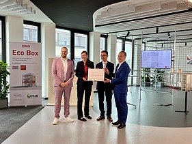 Foto von vier Personen die schick gekleidet sind. Sie halten ein Zertifikat. 