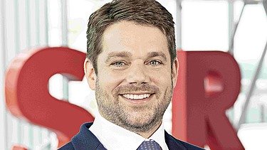 Photo of Klemens Haselsteiner standing in front of the red letters STRABAG