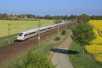 Foto einer Bahnstrecke mit einem weißen Schnellzug, links und rechts blühende, gelbe Rapsfelder