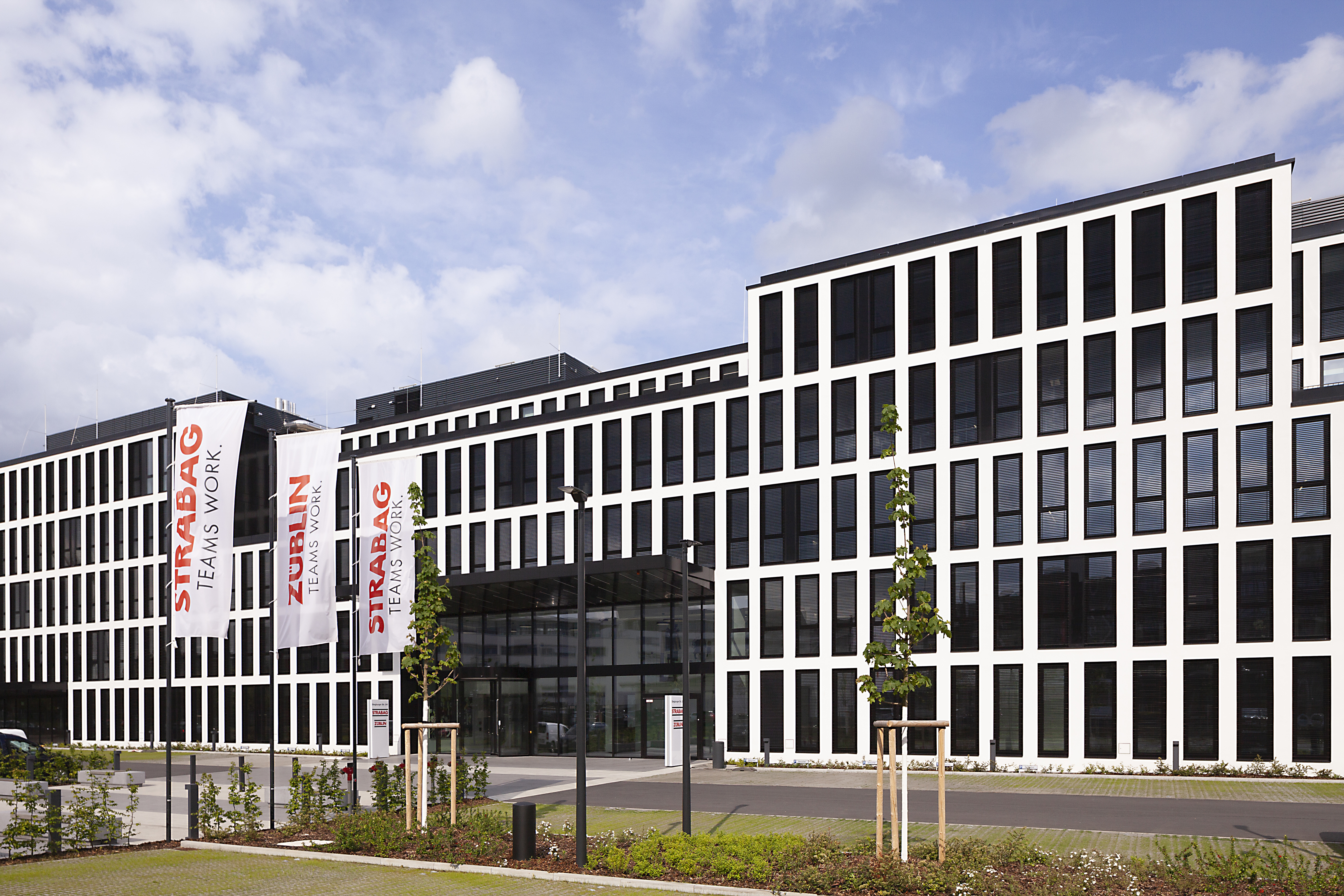 Das Foto zeigt das neue Konzernhaus in Köln, ein modernes Gebäude, fünstöckig mit vielen Feinstern, davor eine Grünfläche