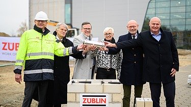 Foto von mehreren Personen, die eine Röhre halten zum Richtfest.  