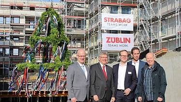 Foto von freundlich schauenden Männern auf einer Baustelle, beim hissen des Richtkranzes.  