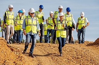 Foto von mehreren Personen in Schutzwesten und Bauhelmen, die auf einem Erdhügel stehen