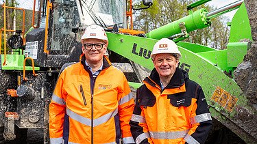 Two men in work clothes standing in front of a wheel loader