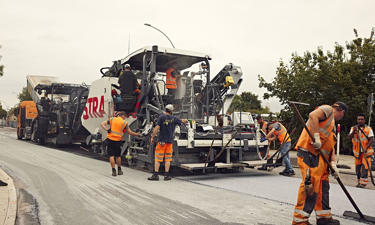 Foto von mehreren Straßenbauarbeitern rund um eine große Asphaltbaumaschine