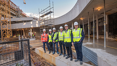 Foto von mehreren Personen mit Bauhelmen und Schutzwesten in einer Baustelle
