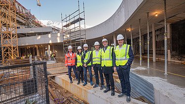 Foto von mehreren Personen mit Bauhelmen und Schutzwesten in einer Baustelle