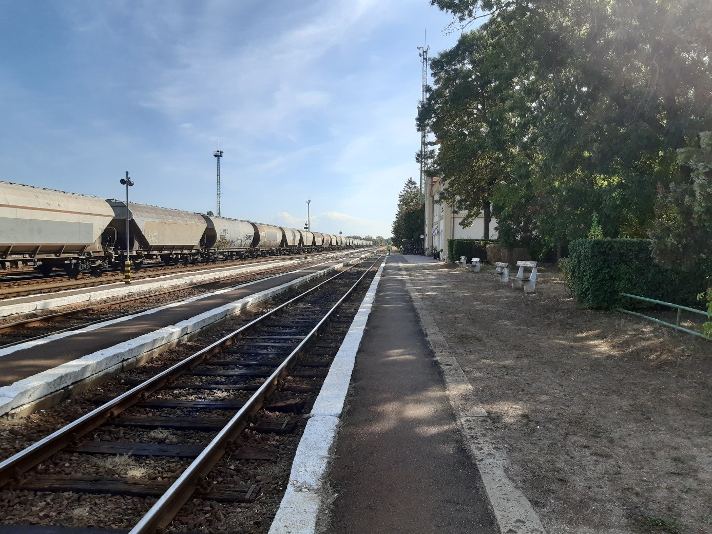 Foto von Bahngleisen bei blauen Himmel, auf einem Gleis steht ein Güterzug mit Waggons