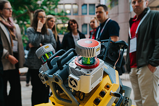 Photo shows an engine in the foreground, behind it some people are looking at it