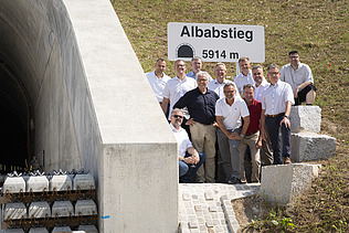 Foto von freundlich schauenden Männern, die neben einem Tunell stehen. 