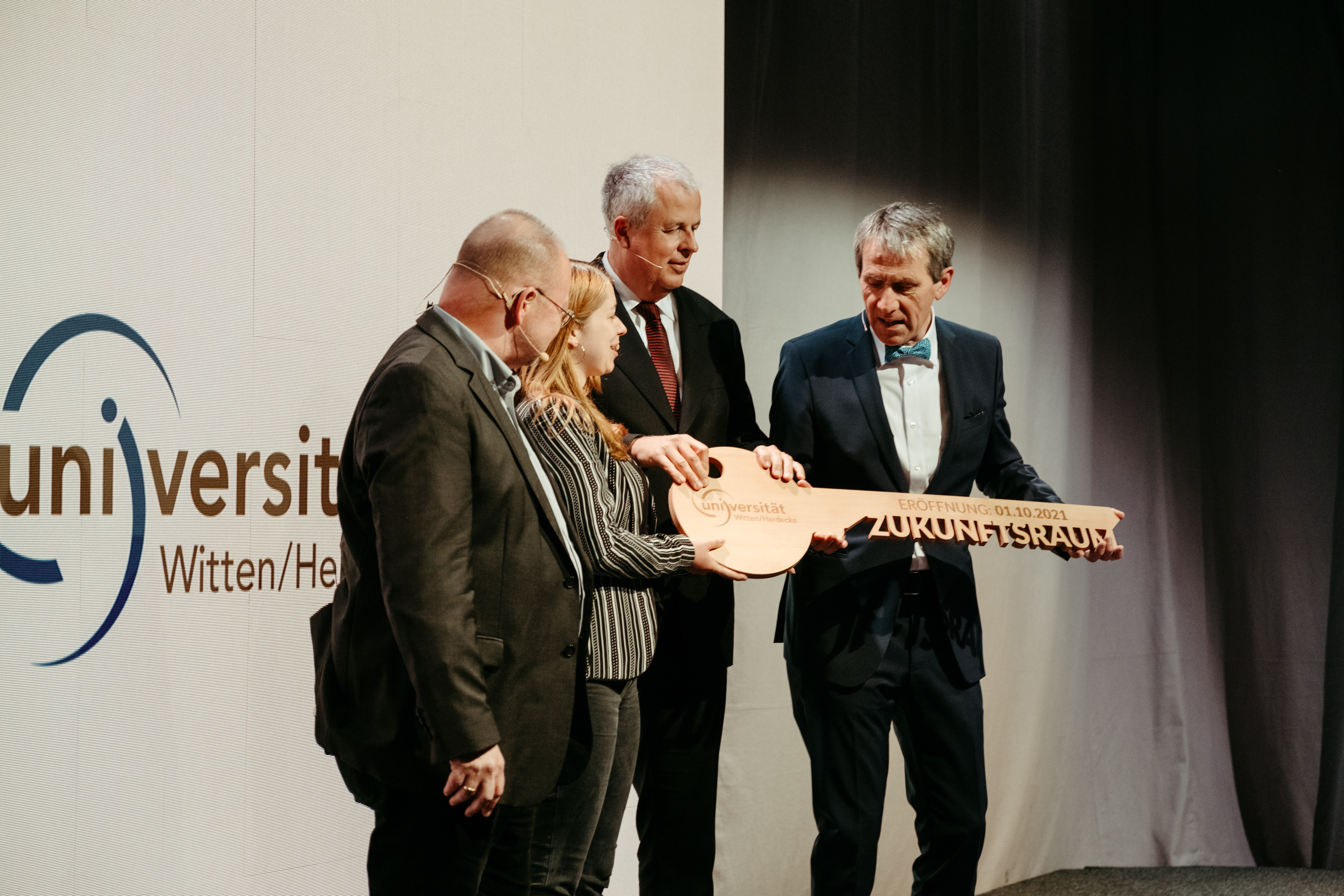Foto von vier Personen die den Schlüssel zur Universität halten.  
