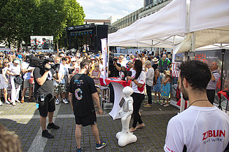 Foto von einem ZÜBLIN-Stand, wo ein Roboter gefilmt wird. Drumherum sind viele Personen versammelt    
