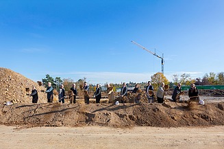 Foto von mehreren Männern auf einer Baustelle die mit einen Sparten Erde in die Luft werfen. 