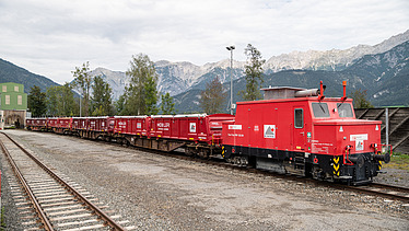 Foto von Bahnschienen, auf dem rechten Gleis steht eine rote Zugmaschine mit Waggons
