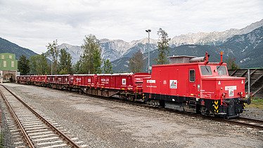 Foto von Bahnschienen, auf dem rechten Gleis steht eine rote Zugmaschine mit Waggons