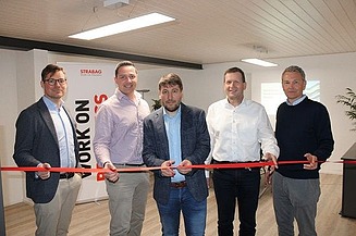 Foto von fünf Männern die ein rotes Band in einem Büroroaum durchschneiden