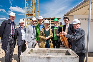 Foto von einer Frau und mehreren Männern auf einer Baustelle, bei symbolischer Grundsein für das JobRad-Firmenzentrale. Ein Mann hält eine Röhre. 