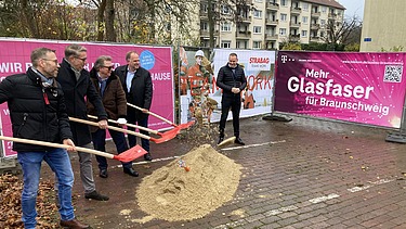 Foto von mehreren Personen beim symbolischen Spatenstich mit Schaufeln in der Hand, dahinter Bautransparente mit der Aufschrift Glasfaser