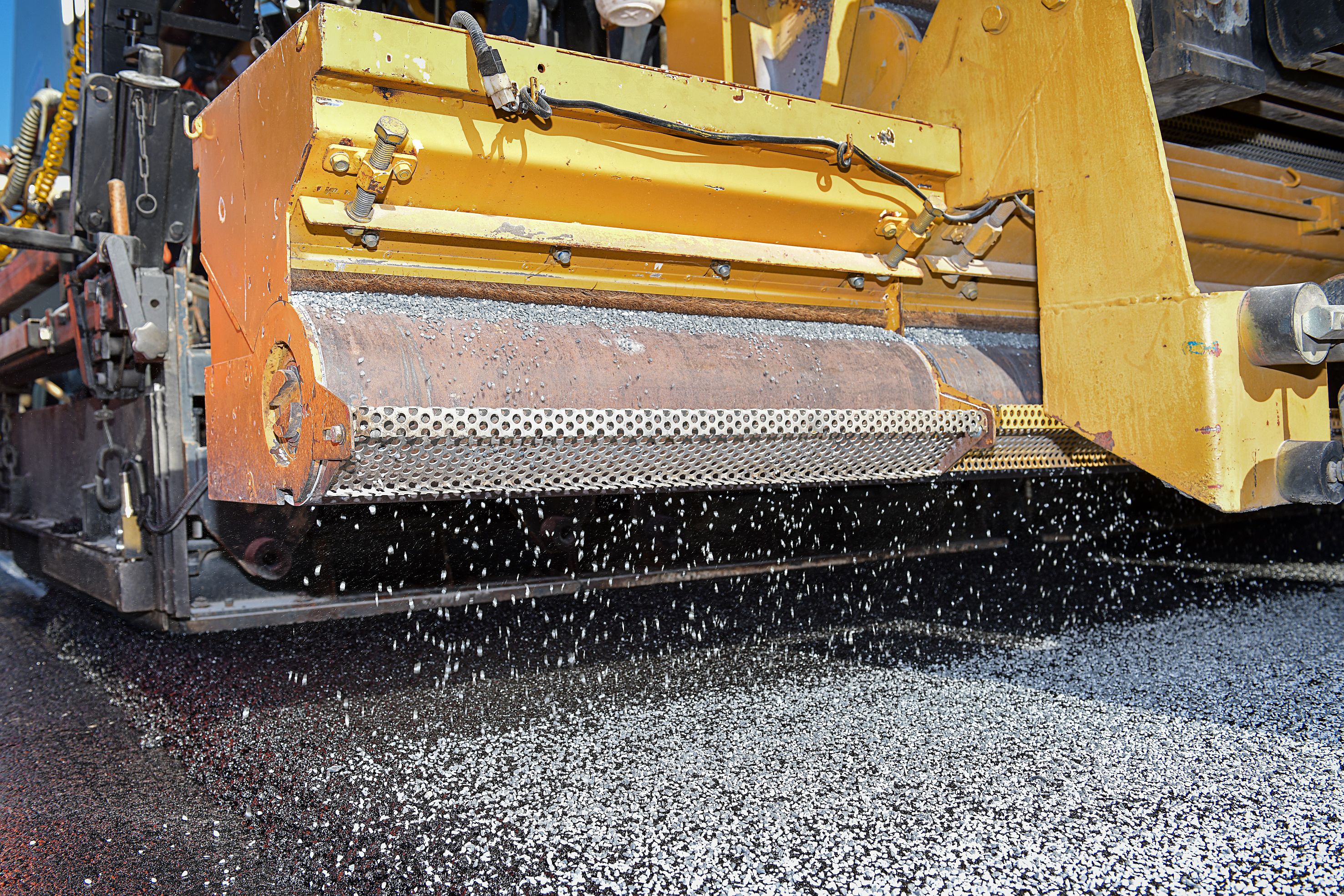 Foto einer Detailansicht einer gelben Asphaltiermaschine bei der Arbeit
