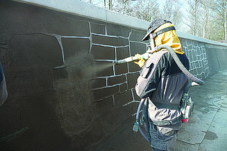  Foto von einer Person, die eine Wand mit brauner Farbe besprüht.