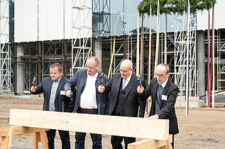 Foto von vier Männern die einen Nagel in ein Holzbrett hauen.  