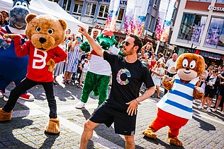 Foto von tanzenden Maskottchen und einem Animator. Drumherum sind viele Menschen.  