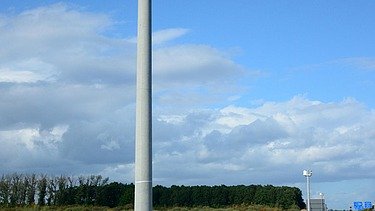 Foto eines Mastes mit einem technischen Gerät auf der Spitze, bei blauem Himmel