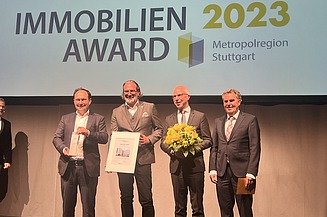 Foto von vier Männern im Anzug die auf einer Bühne stehen. 