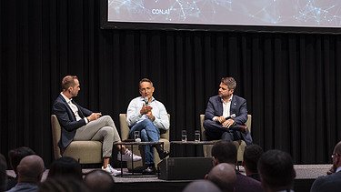 Foto von drei sitzenden Personen bei einer Podiumsdiskussion