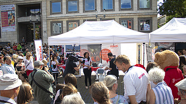 Foto von einem ZÜBLIN-Stand, wo eine Reportage von einem Roboter gedreht wird. Drumherum sind viele Personen versammelt    