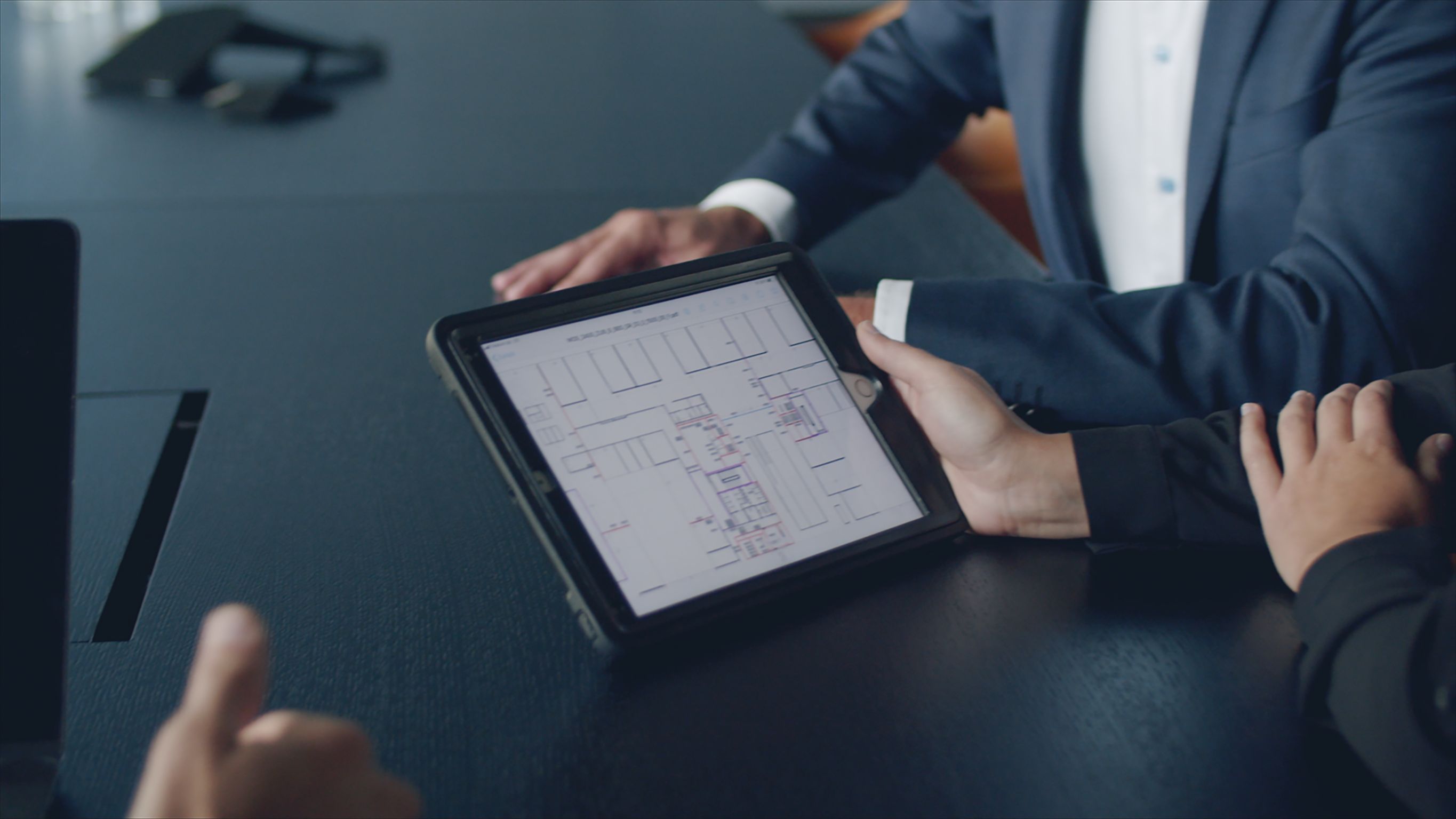 Foto von einem einer Besprechung mit einem Fokus auf ein I-Pad. Auf dem I-Pad ist ein Bauplan zusehen.  