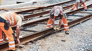 Foto von drei Schienenbauarbeitern beim Schienenverlegen