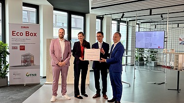 Foto von vier Personen die schick gekleidet sind. Sie halten ein Zertifikat. 