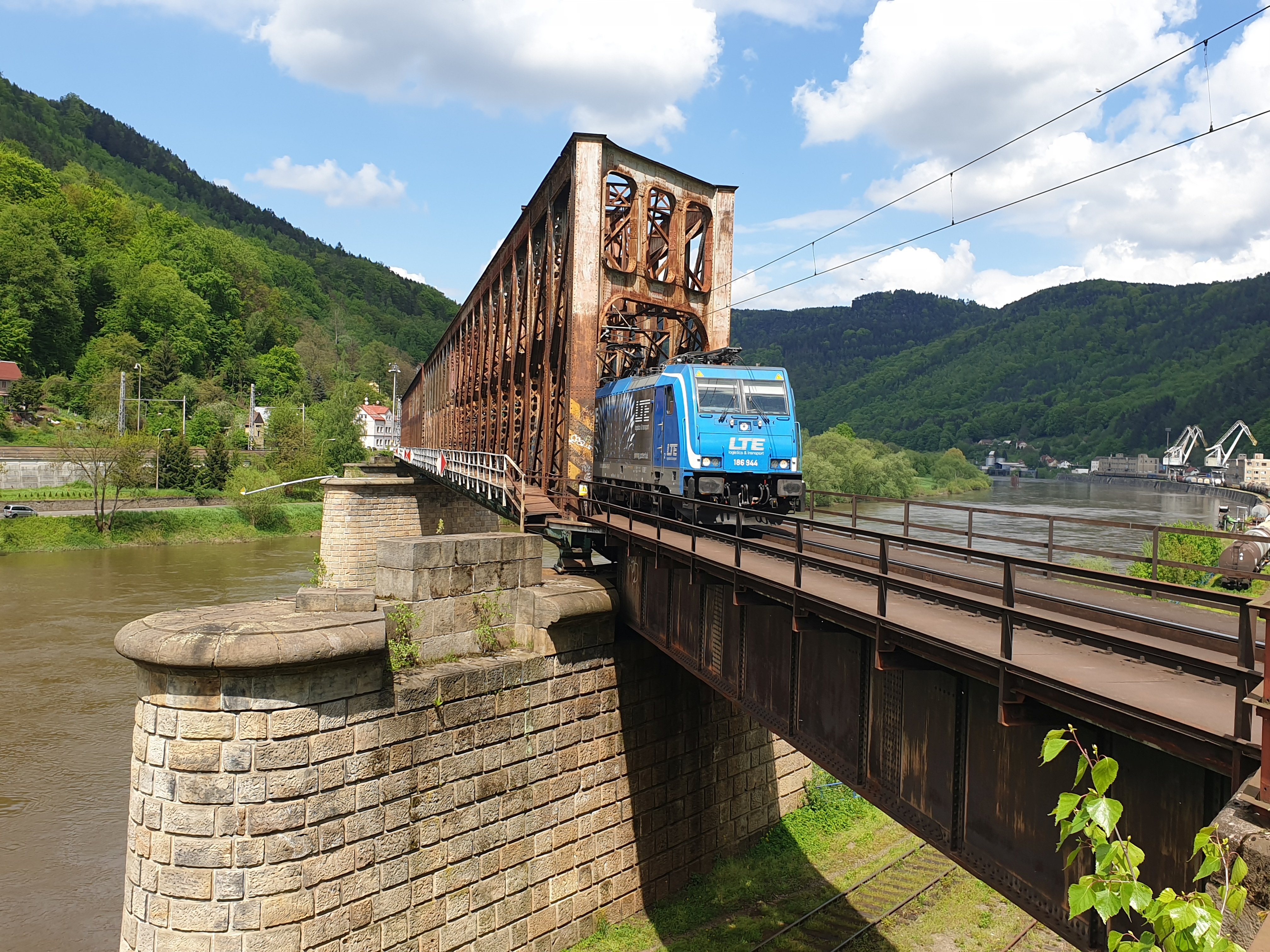 Photo of a railway bridge made of rusty steel with a blue train
