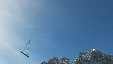 Foto von einem Hubschrauber der Material an einem Seil transportier in einem Gebirge.  