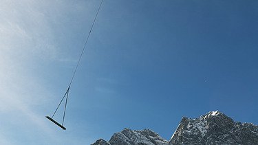 Foto von einem Hubschrauber der Material an einem Seil transportier in einem Gebirge.  