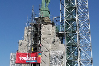  Foto von einer hochgebauten Statue, die auf einem Podest steht. Um das Podest ist ein Gerüst aufgebaut ist.