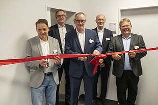 Foto von mehreren Personen die ein Einweihungsband durchschneiden.  