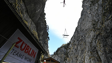 Foto von Hubschrauber, der Material in eine Schlucht abseilt.                 