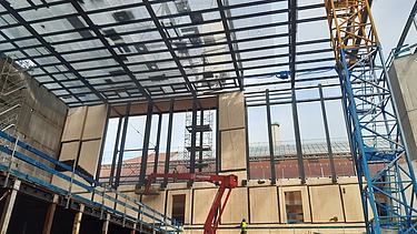 Foto von einer Baustelle von innen. Es ist ein Kran und Hebebühnen zusehen. 