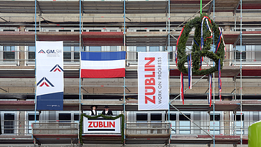 Foto von zwei Personen, die auf einem Gerüst stehen und den Richtspruch verkünden. 