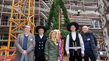 Fünf freundlich schauende Person stehen vor einem Richtfest 