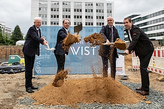 Foto von vier Männern, die mit einem Spatzen, Erde von einem Haufen Erde hochwerfen.  
