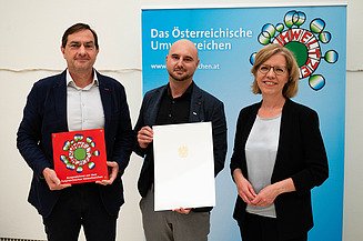 Foto von drei Personen, die beiden links halten jeweils eine Urkunde in den Händen